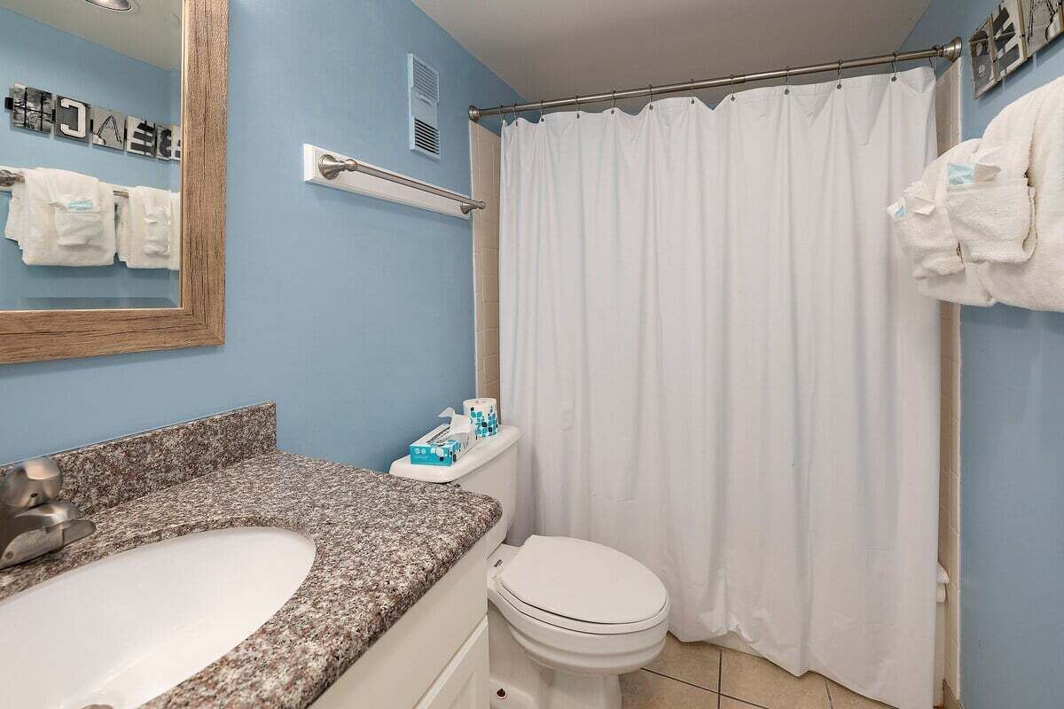 A bathroom with a granite countertop sink, a white toilet, a shower curtain, and a towel rack with towels.