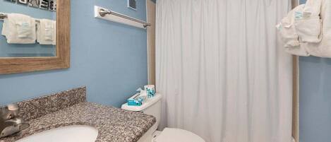 A bathroom with a granite countertop sink, a white toilet, a shower curtain, and a towel rack with towels.