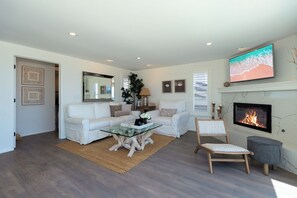 A living room with a white sofa, a glass coffee table, a fireplace, and a television mounted on the wall.