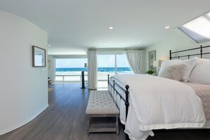 Quarto com cama grande, um banco e vista para o oceano, além de um claraboia.