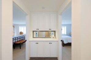 A hallway with a white door at the end leading to a bedroom with a bed and a window.
