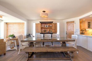 Uma área de refeições com mesa de vidro, cadeiras de vime e um banco de madeira.