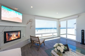 Uma sala de estar ampla com lareira, uma televisão grande e vista para a praia.