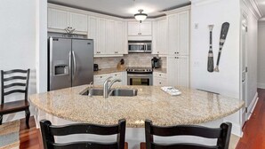 A kitchen with white cabinets, a granite countertop island, stainless steel appliances, and a ceiling light fixture. - Breathtaking Views of the Inter-coastal Waterway (Saint Simons Island)