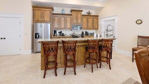 Una cocina con armarios de madera, un refrigerador de acero inoxidable, un microondas y una cafetera. Hay cuatro taburetes de bar de madera en la isla.