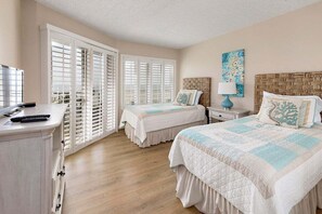 A hotel room with two beds, a desk, and a window with shutters.