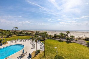 A swimming pool with lounge chairs and umbrellas, a grassy area, and a beach in the background. - Spacious and Oceanfront Condo (Saint Simons Island)