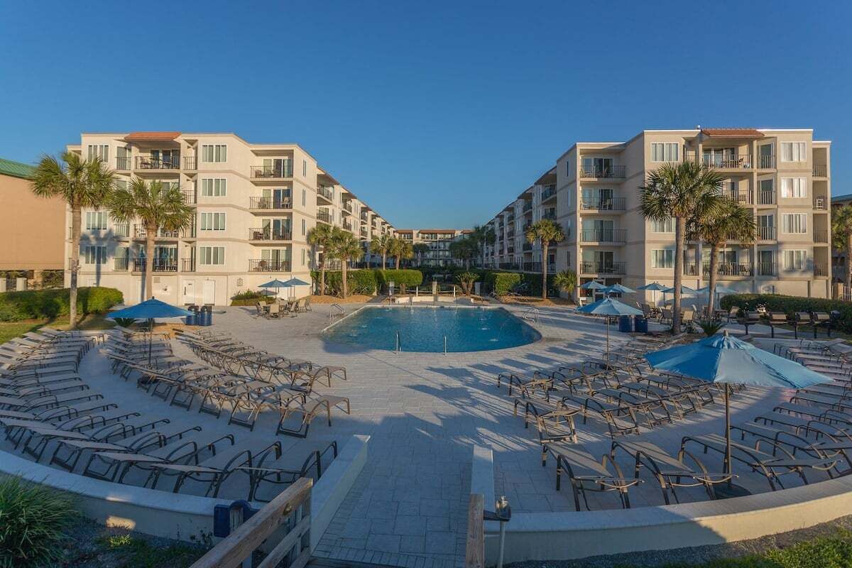 Un hotel con piscina central, varios balcones y zonas de estar al aire libre.