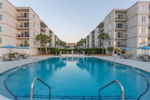 Piscina cercada por um edifício com varandas e áreas de estar ao ar livre.
