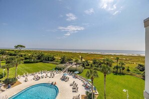A pool area with a view of the beach, surrounded by palm trees and lounge chairs. - Family Friendly Direct Ocean View Condo (Saint Simons Island)