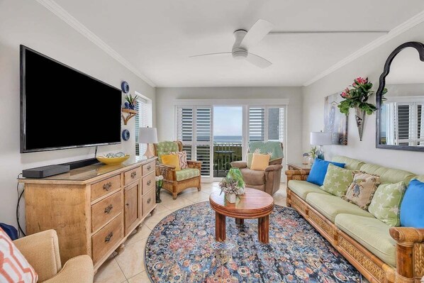 A living room with a flat-screen TV, wooden furniture, a patterned rug, and a balcony with shutters. - Family Friendly Direct Ocean View Condo (Saint Simons Island)