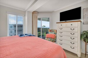 A bedroom with a large bed, a dresser, a television, and a balcony with a view. - Family Friendly Direct Ocean View Condo (Saint Simons Island)