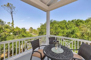 A covered outdoor seating area with a table and chairs, overlooking a lush green landscape. - Ocean Views with Swimming Pool. (Saint Simons Island)