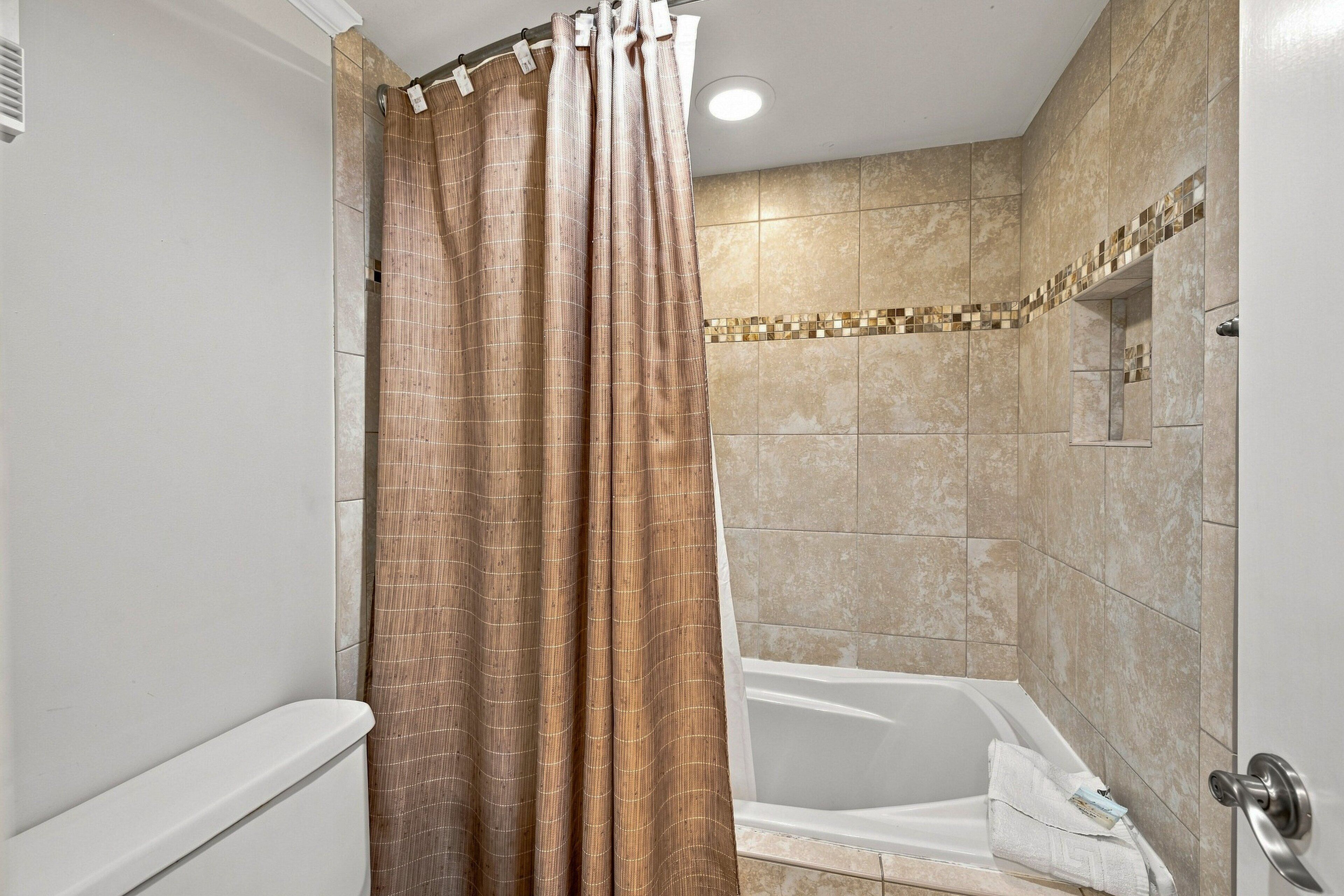 A bathroom with a shower curtain, a bathtub, and tiled walls.