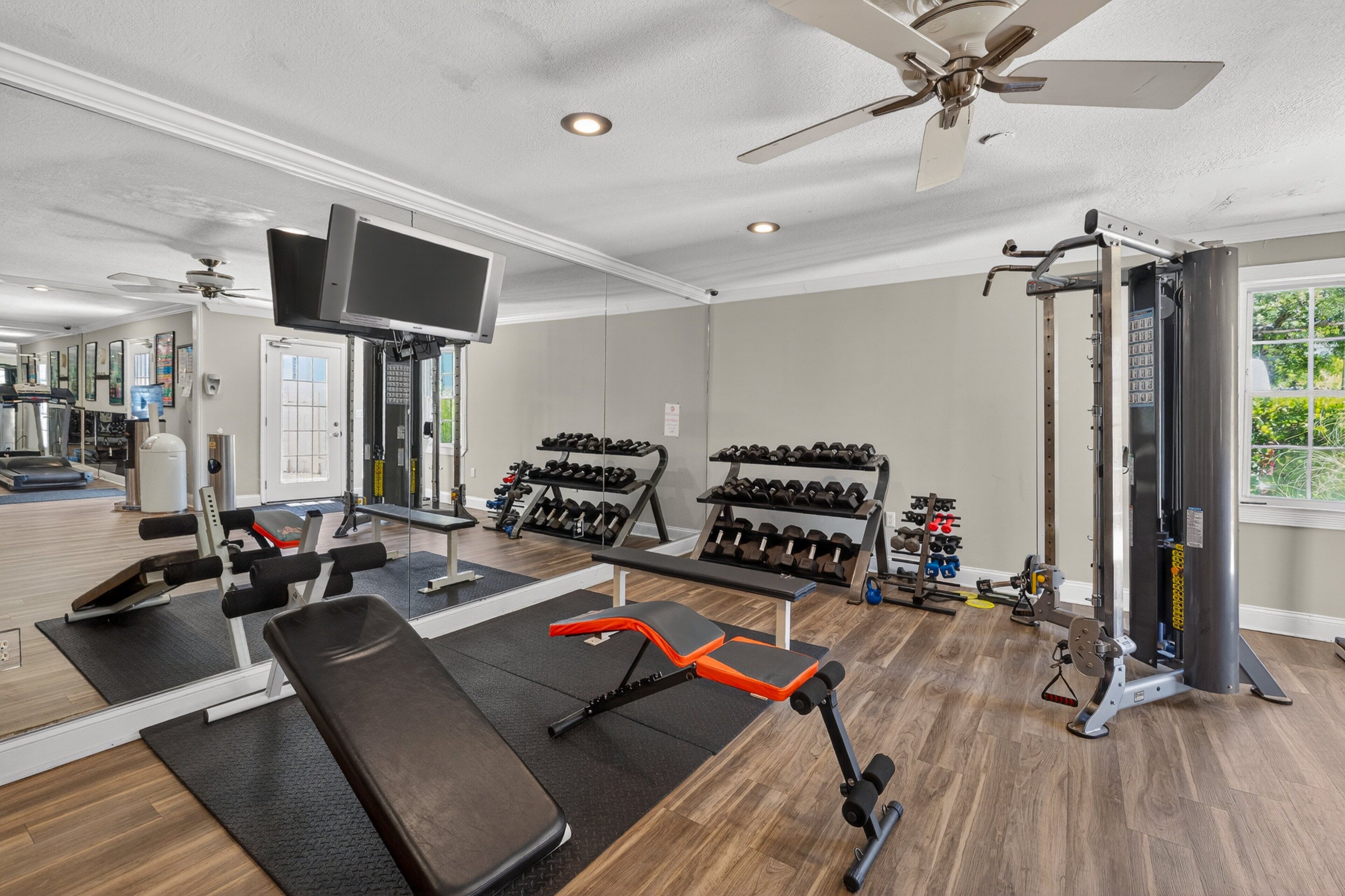 A gym with exercise equipment, a television, and a ceiling fan.