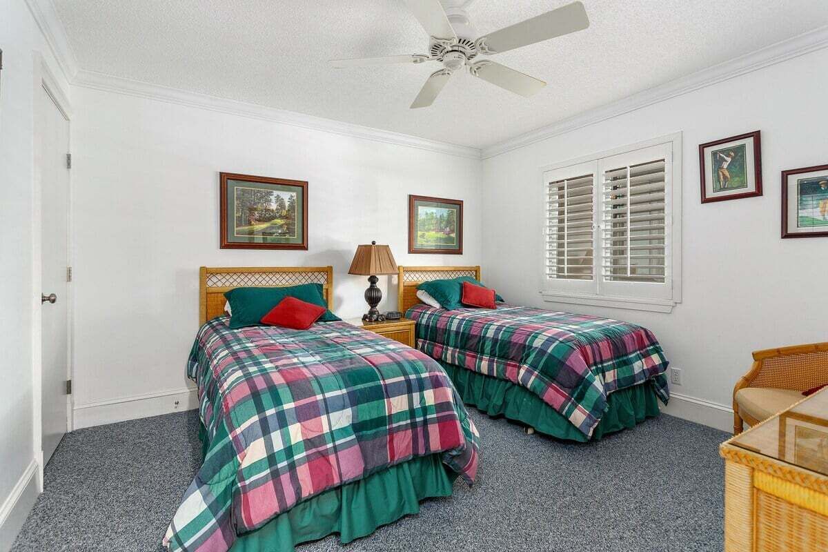 A bedroom with two beds, a ceiling fan, and a window with shutters.