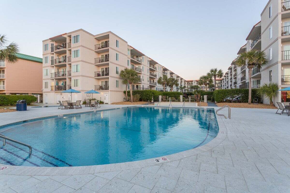 Une piscine entourée d’immeubles résidentiels à plusieurs étages, dotés de balcons, de coins salon extérieurs et de palmiers.