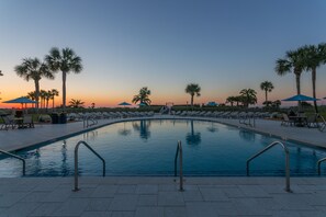 Relax by the serene pool surrounded by palm trees and lounge chairs.