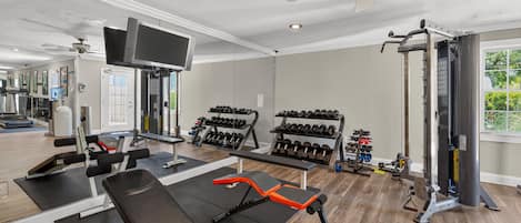 A gym with exercise equipment, a television, and a ceiling fan.