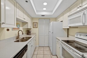 A compact kitchen with white cabinets, a double sink, a refrigerator, and a stove. - Oceanfront Condominium with Great Amenities (Saint Simons Island)