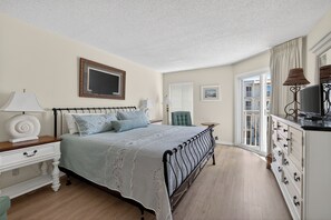 A bedroom with a bed, bedside table, lamp, dresser, and a view of the outside balcony. - Oceanfront Condominium with Great Amenities (Saint Simons Island)