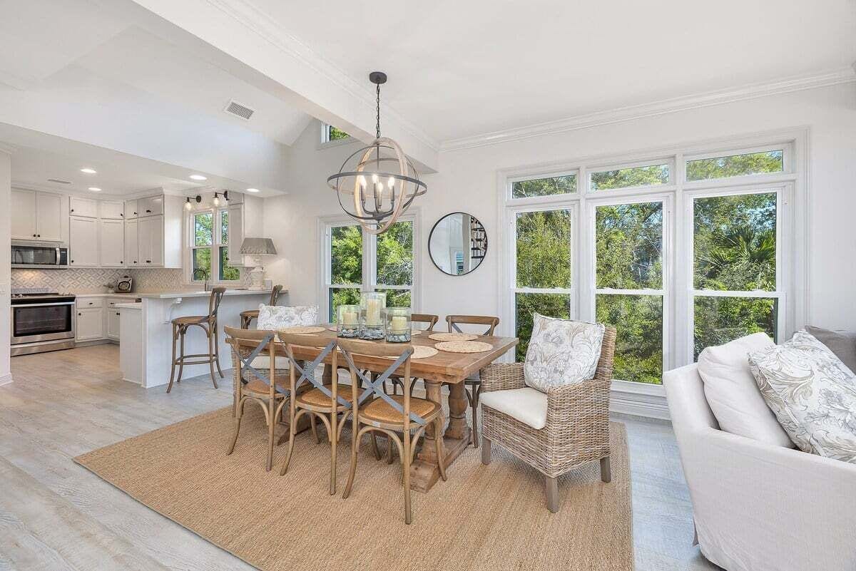 A spacious kitchen with white cabinetry, a dining area with a round table and chairs, and a large window offering a view of greenery.