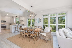 A spacious kitchen with white cabinetry, a dining area with a round table and chairs, and a large window offering a view of greenery.