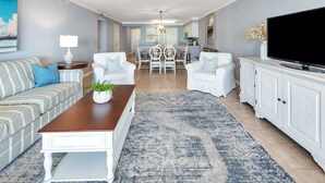 A living room with a sofa, two armchairs, a coffee table, a TV, and a dining area with a table and chairs. - Oceanfront Condo in the Heart of The Village. (Saint Simons Island)