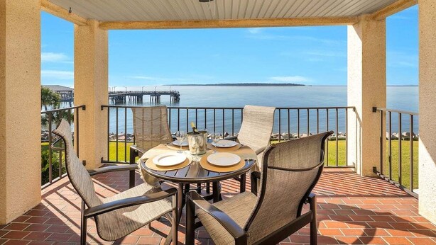 A covered outdoor patio with a table set for two, overlooking a body of water and a pier. - Oceanfront Condo in the Heart of The Village. (Saint Simons Island)