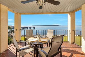 A covered outdoor patio with a table set for two, overlooking a body of water and a pier. - Oceanfront Condo in the Heart of The Village. (Saint Simons Island)