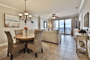 Cozy living room with a round dining table, wicker chairs, and a chandelier. Enjoy the view from the large window and relax with a ceiling fan.