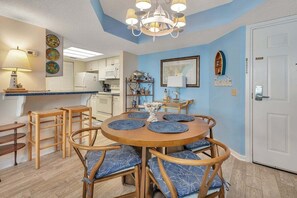 A dining area with a round wooden table, blue cushioned chairs, and a chandelier.