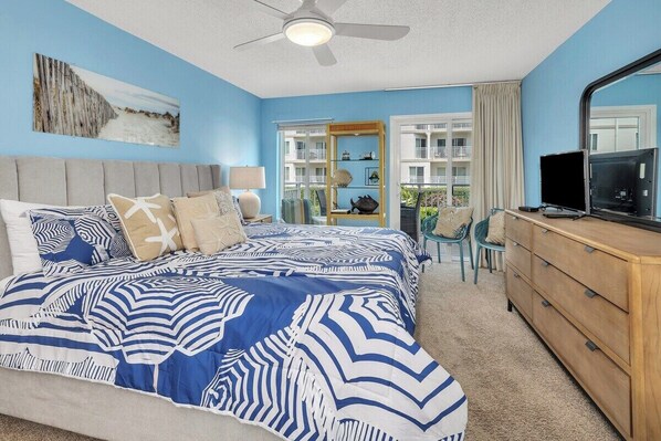 A bedroom with a bed, a dresser, a ceiling fan, and a window with a view of a building.