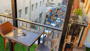 Un balcon avec une table et des chaises, une vue sur une rue animée en contrebas et une plante en pot.