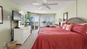 Une chambre avec un grand lit, un ventilateur de plafond, une télévision, une commode et un balcon avec vue.