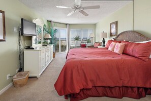 Ein Schlafzimmer mit einem großen Bett, einem Deckenventilator, einem Fernseher, einer Kommode und einem Balkon mit Blick.