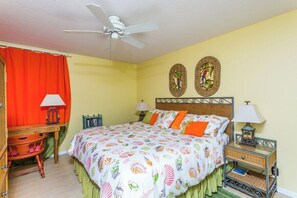 Une chambre à coucher comprenant un lit, deux tables de chevet, un bureau et un ventilateur de plafond.