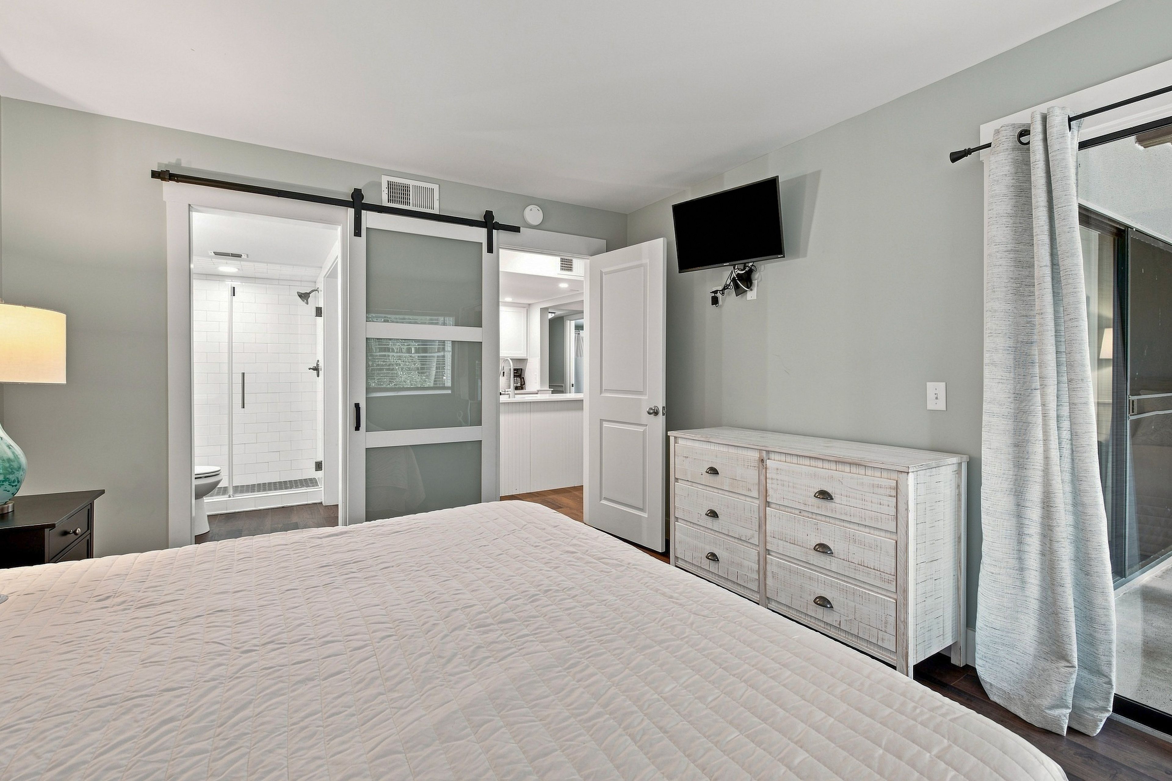 Een slaapkamer met een bed, een dressoir, een televisie en een badkamer met douche en toilet.