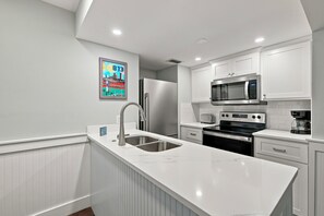 A modern kitchen with white cabinetry, a stainless steel refrigerator, a built-in microwave, and a double sink. - Oceanfront Condominium with Balcony and Pool (Saint Simons Island)