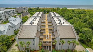 A modern building with a central courtyard, surrounded by lush greenery and a view of the ocean. - Oceanfront Condominium with Balcony and Pool (Saint Simons Island)