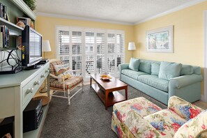 Relax in this inviting living room with a sofa, ottoman, and armchair, perfect for unwinding near a vintage TV and a beautiful window.