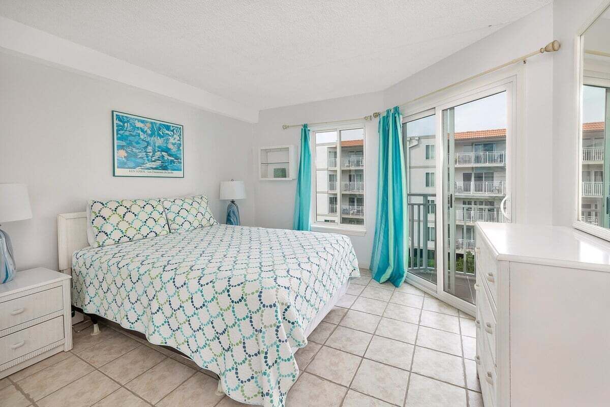 Une chambre à coucher comprenant un lit, une table de chevet, une commode, une fenêtre avec des rideaux et un balcon avec vue.