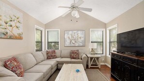 A living room with a sectional sofa, a coffee table, a TV, and artwork on the walls. - Enjoy being steps from the Pier Village at #508! (Saint Simons Island)