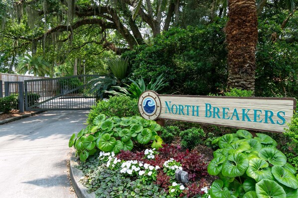 A sign for 'North Breakers' with a wooden board, surrounded by lush greenery and a palm tree.
