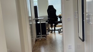 A hallway with a grey tufted ottoman, a desk with a computer, a black office chair, and a set of dumbbells on the floor. - Room King siz Bed 5 Min Train Arlanda 17 min (Knivsta)