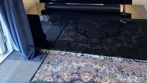 A flat-screen TV on a black stand in a room with a patterned rug and a window with curtains. - Room King siz Bed 5 Min Train Arlanda 17 min (Knivsta)