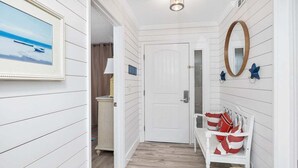 A hallway with white wooden walls, a white bench with red and white striped cushions, a wooden door, and a framed picture on the wall. - Oceanfront Condominium with Pool. Pet Friendly. (Saint Simons Island)