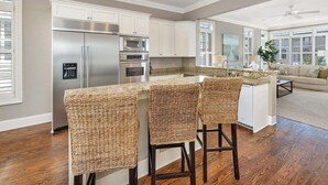 Una cocina moderna con armarios blancos, electrodomésticos de acero inoxidable y una zona de bar con sillas de mimbre.