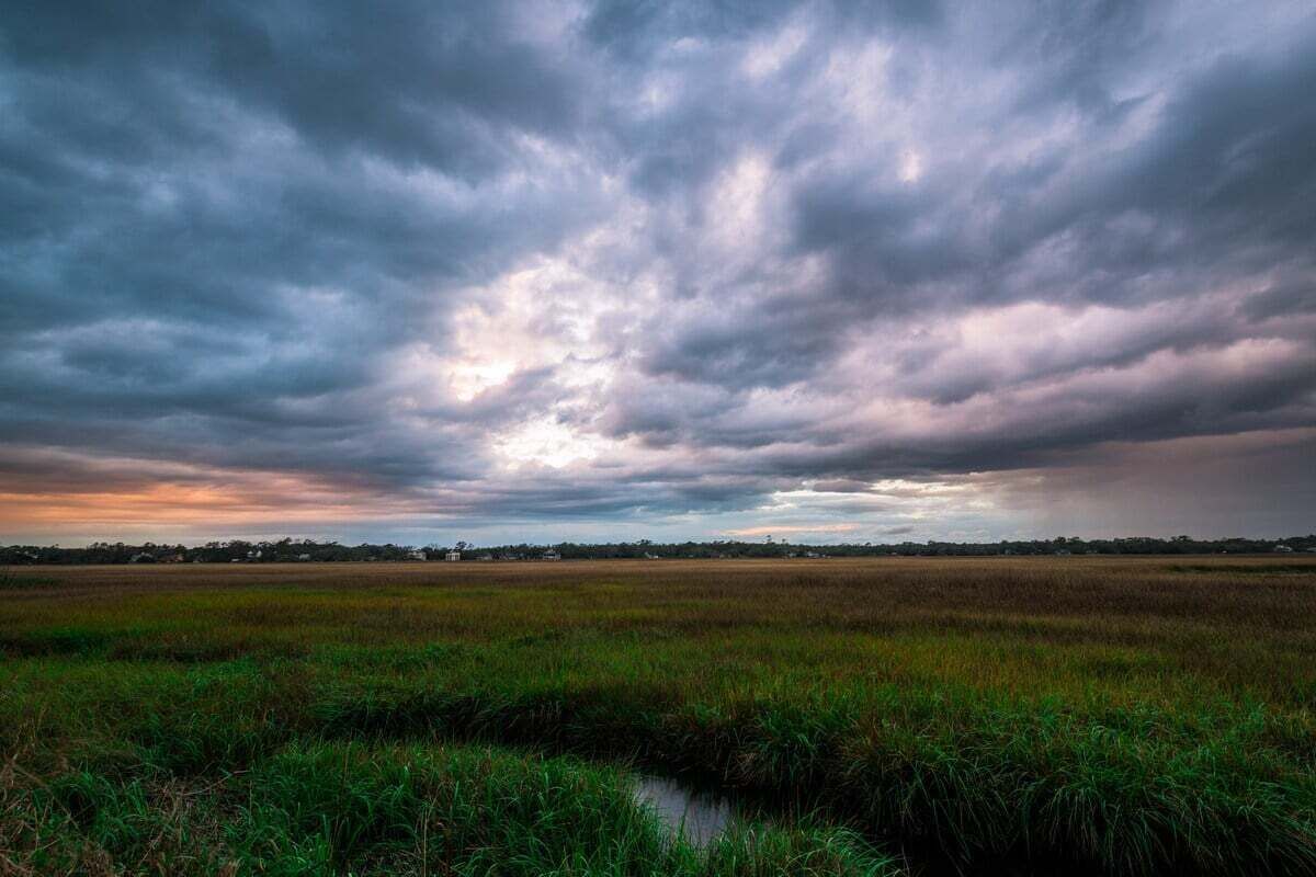 A flat landscape with a water body in the foreground and a cloudy sky above.