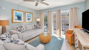 A living room with a sofa, armchairs, a coffee table, a TV, and a balcony with curtains. - Beachfront Condominium Perfect for Small Families! Pool, Fitness Center, Tennis! (Saint Simons Island)